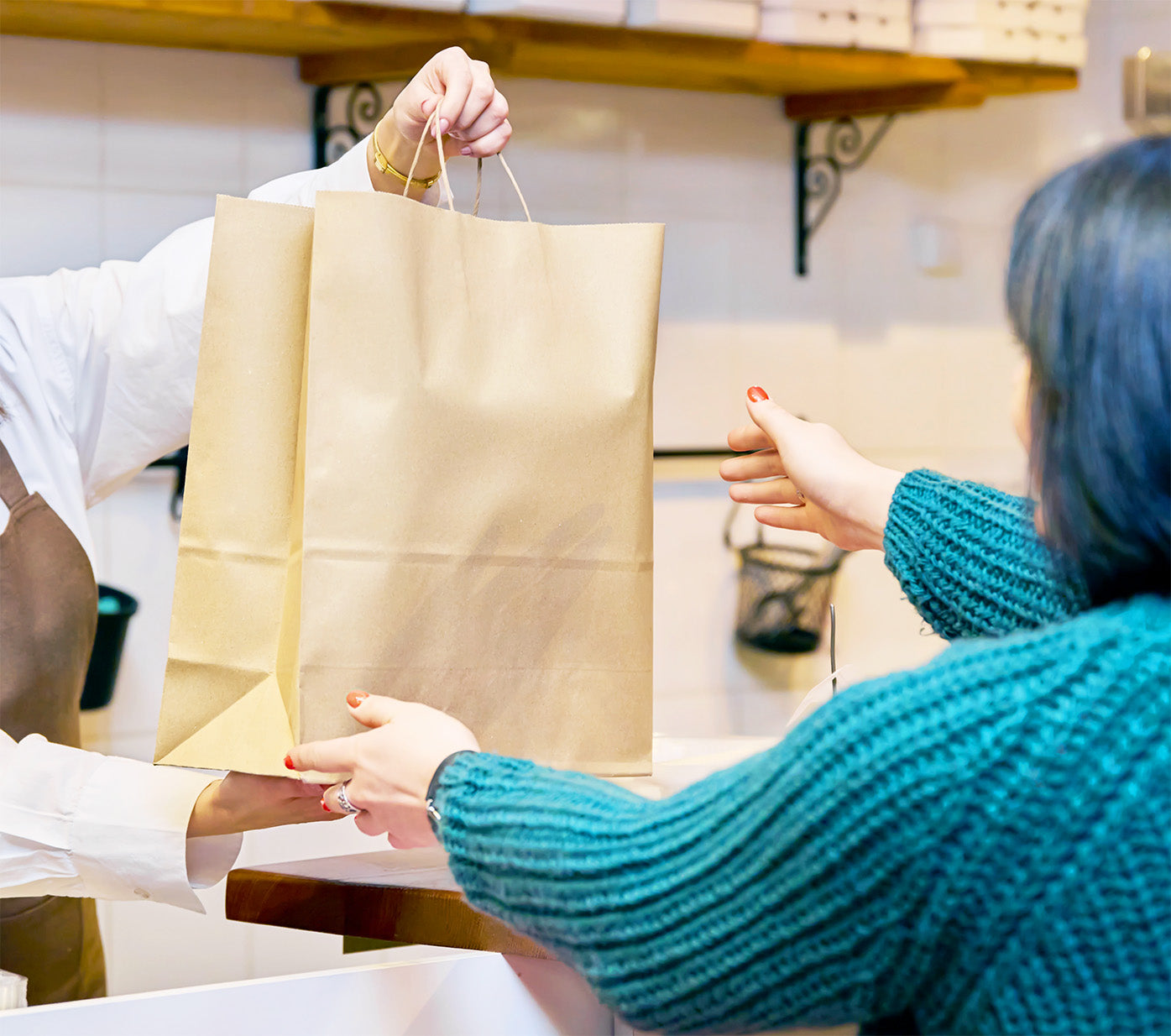Een vrouw met een blauwe trui neemt een bestelling in een papieren zak aan.